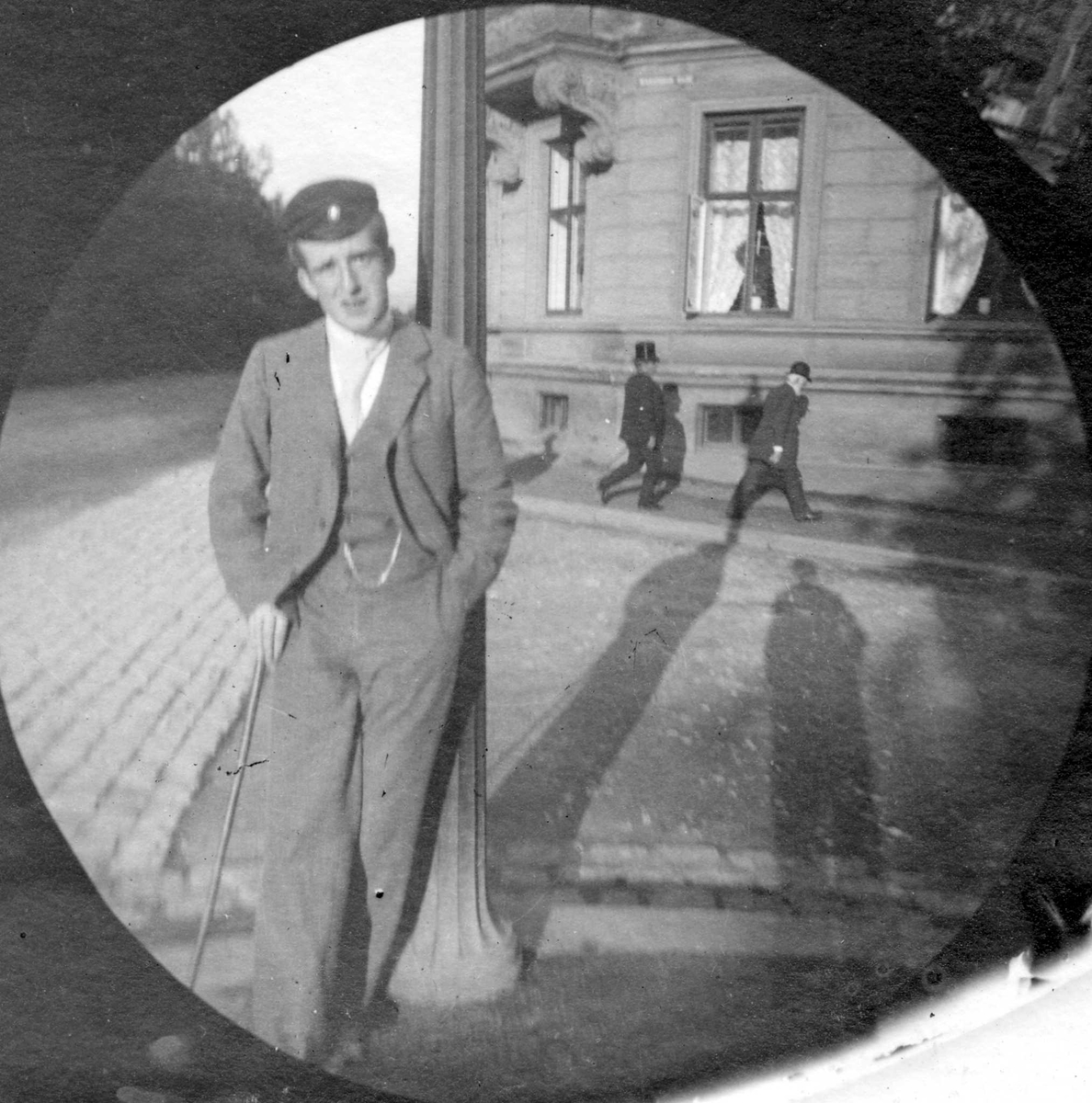 Student Bilten (?) Hiorthdal står lent mot lyktestolpe i gatekryss med bygård bak, Oslo. Student fra 1892.