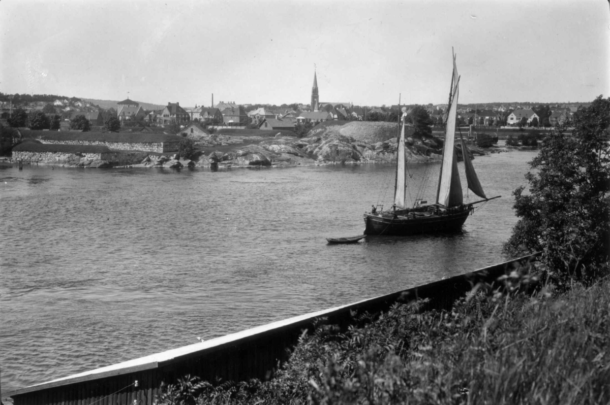 Fredrikstad, Østfold. 1930. Oversiktsbilde med elv og seilskute i forgrunnen. Bebyggelse med kirke i bakgrunnen.