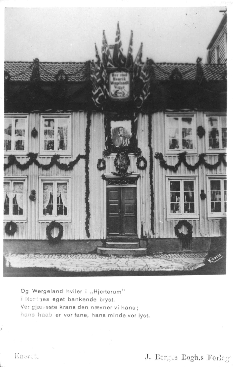 Postkort. Henrik Wergelands fødested, huset er dekorert med kranser, flagg og portrett i anledning jubileet.