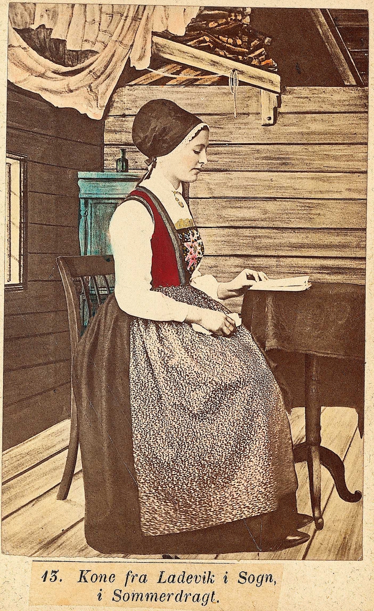 13. Konedrakt, sommer, Lavik, Høyanger. Portrett av sittende kvinne plassert i tegnet stueinteriør. Hun leser i en bok.( Samme motiv som nr.12. Nr. 13, jfr. NF.09403-001 viser annen drakt på samme kvinne i samme interiør.)
Fra serien "Norske Nationaldragter" (nr.13), visittkortformat, håndkolorert. Serien er fotografert av fotograf Marcus Selmer (1819-1900), Bergen.