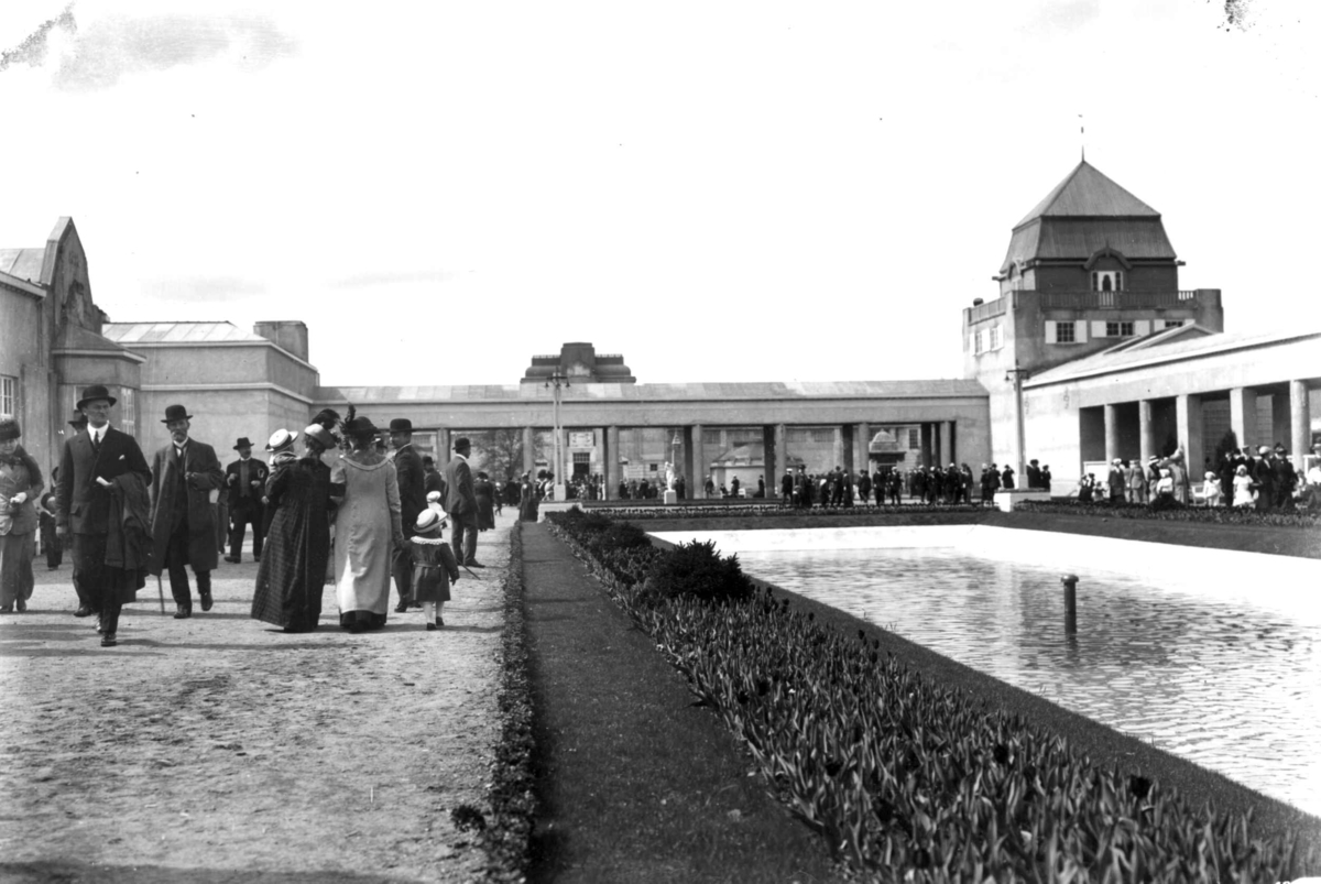 Jubileumsutstillingen på Frogner, Oslo, 1914.
Frogner Hovedgård med Bergen bys paviljong til venstre. Publikum spaserer på området. Basseng til høyre. Blomsterbed langs kanten.
