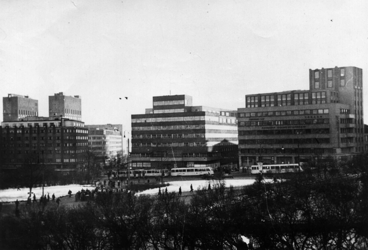 Gatebilde med busser og bygninger. På baksiden av bildet står: "Tre tyske høyborger i Oslo. Til venstre på bildet sees tårnene av Rådhuset med militære anlegg på toppen. Midt på bildet ligger Odd Fellow-bygningen, hovedsetet for Reichkommissaren og til høyre Torstedbygget med kontorer for Der Høhere SS und Polizeiführer, der Reichskommissar, Standorten-Kommandantur der SS Reichskommissar der Seeschiffahrt, m.m."