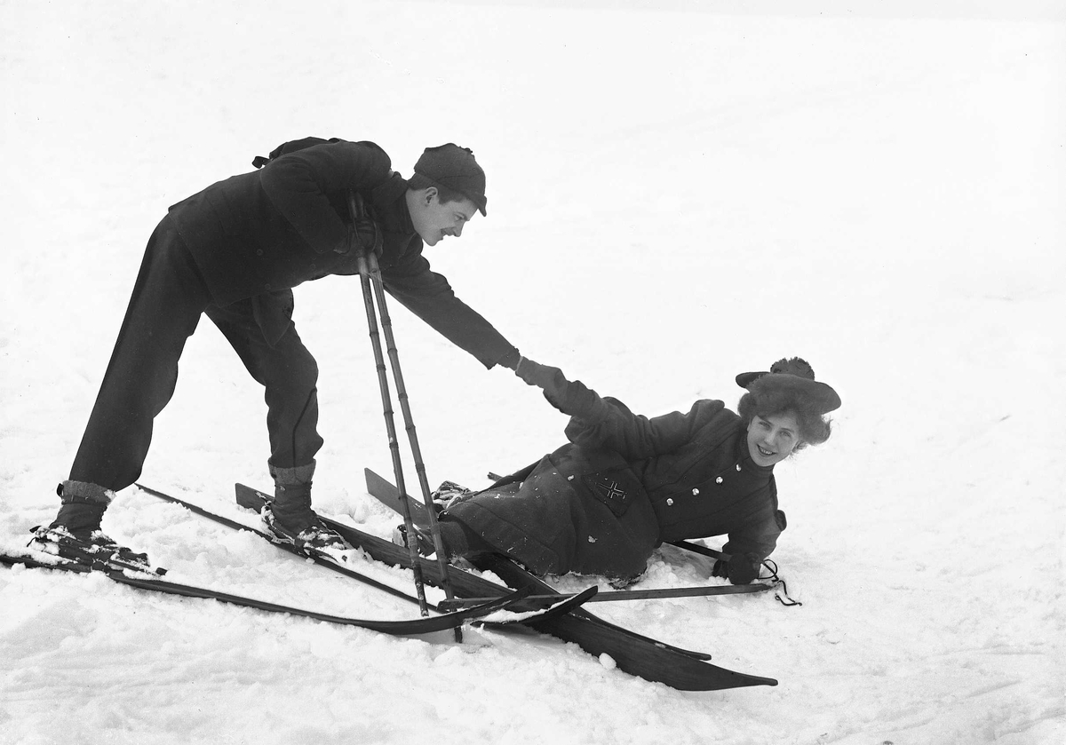 Kvinne og mann på ski i snødekt landskap. Mannen hjelper kvinnen opp etter et fall.