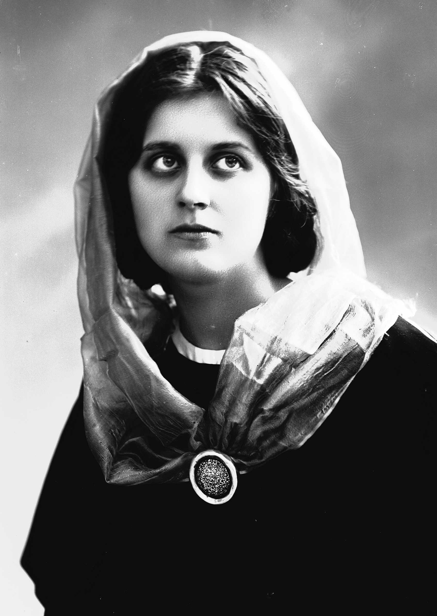Studioportrett av kvinne i drakt og sjal, med brosje i halsen.
