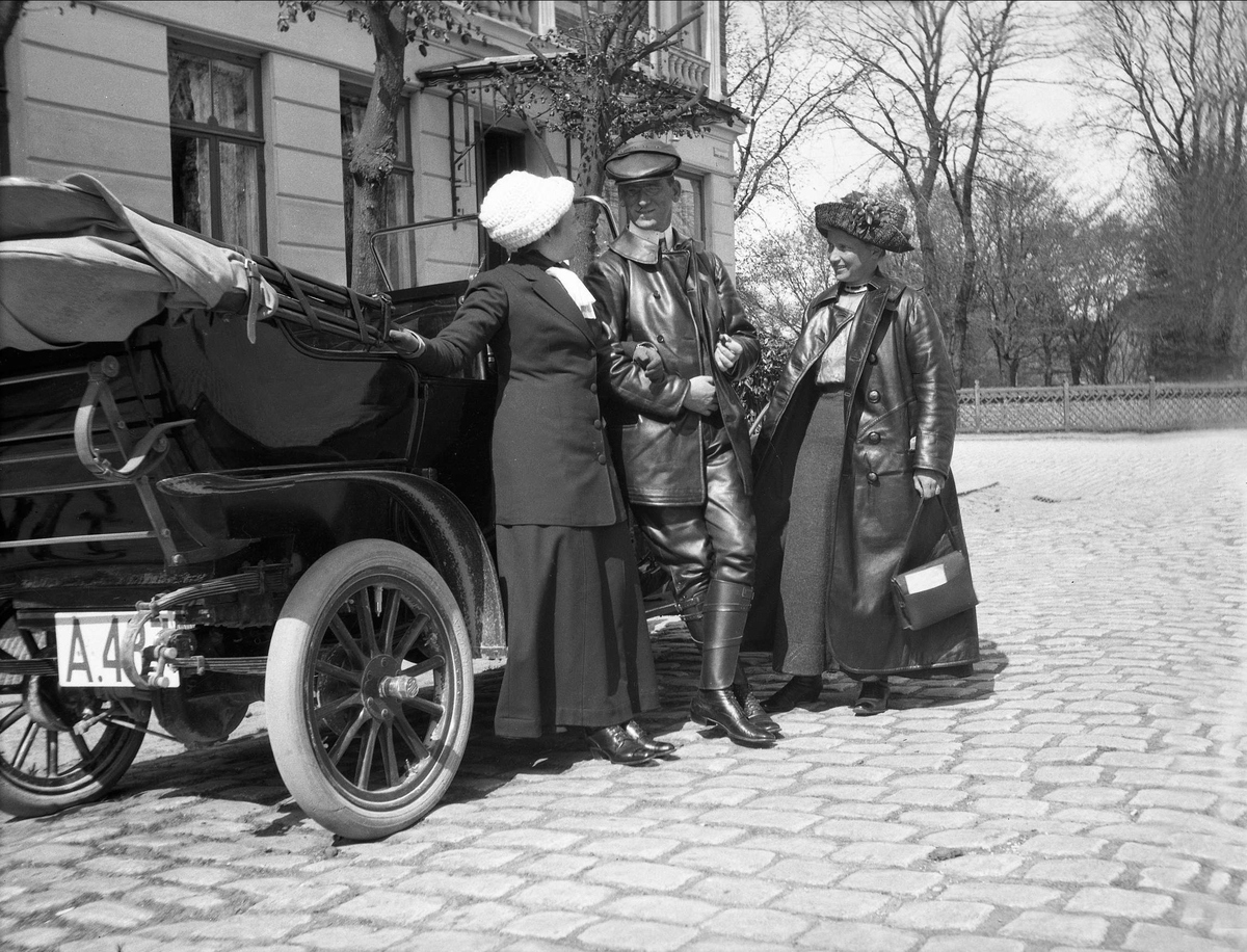 En mann står imellom to kvinner, de lener seg mot en åpen bil. Robsahm og Lund.