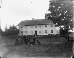 Gruppeportrett, persongruppe foran våningshus, ukjent sted.