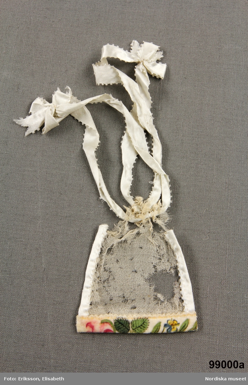 Inventering Sesam 1996-1999:
a) L 9 cm, B 8 cm
b) 9 x 9 cm
a) dockväska, redicule, med sidor av tunn, vit cr¿pe (endast fragment kvar), nederkant av sammet med blommotiv, dragsko av långa vita sidenband med rosetter. Trol. 1820-tal.
b) docknäsduk av vit bomull med knypplad spets runt kanterna. 
Hör till dockan "Julie"  inv.nr. 98.987
Bilaga ="Har haft till egarinnor fru Louise Sterky, född Sterky, och Carin Sterky, född Sterky, döttrar till grosshandlare Fredrik Sterky, Stockholm."
Leif Wallin dec 1996
