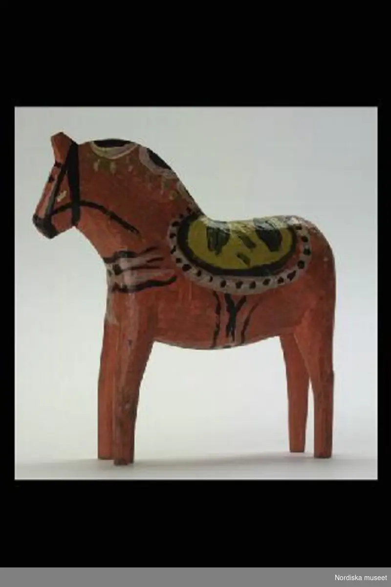 Inventering Sesam 1996-1999:
L 17  H 17,5 B 4 (cm)
Häst av skuren trä, målad i orange färg med krusning i gult, grönt och vitt. Tillverkad 1937 av Tysk Anders Gunnarsson "Gambel-Dammen", Nusnäs.
Birgitta Martinius 1996