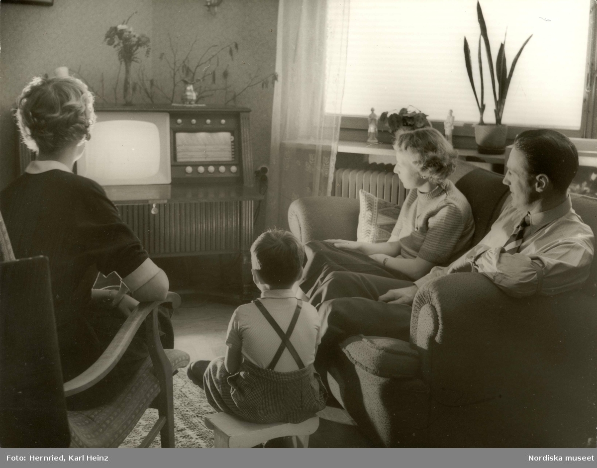 Barn och vuxna tittar på TV på en kombinerad TV- och radiomöbel i vardagsrum.