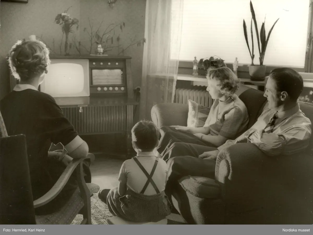 Barn och vuxna tittar på TV på en kombinerad TV- och radiomöbel i vardagsrum.