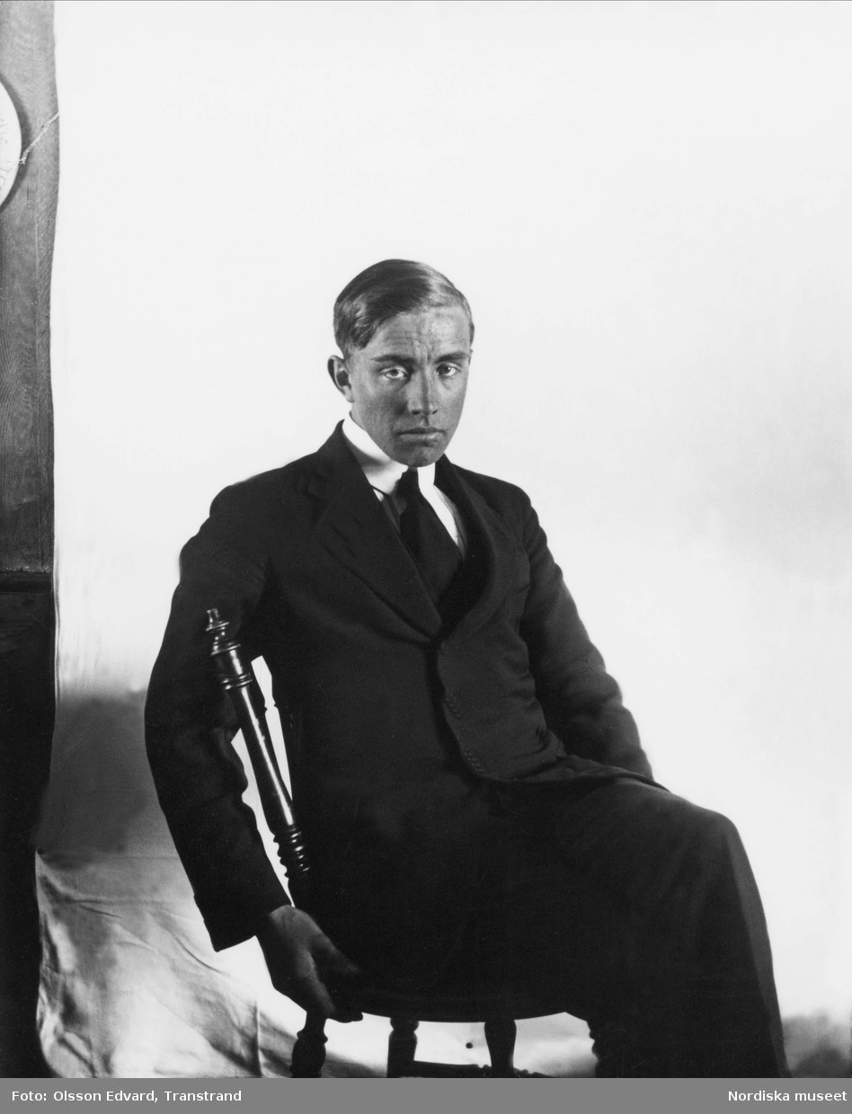 Edvard Olsson klädd i mörk kostym och med sidbenat hår sitter på en stol. Självporträtt.