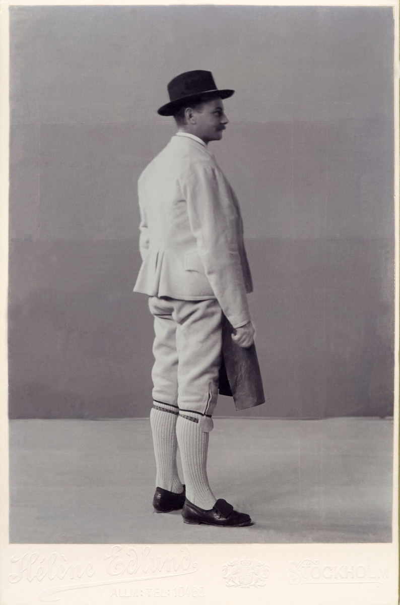 Man i profil klädd folkdräkt från Dalarna med hatt, kort jacka, knäbyxor och skinnförkläde.
