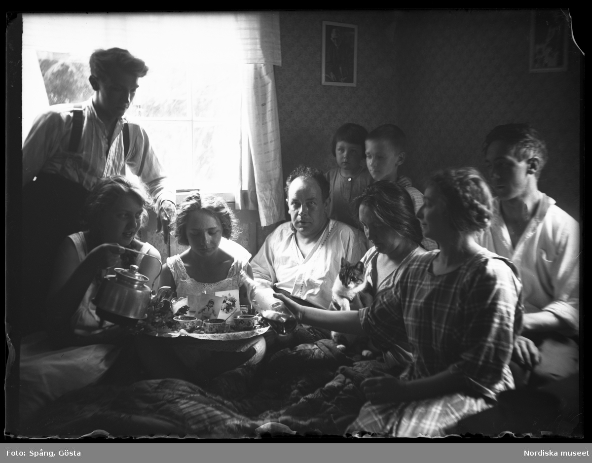 Familj uppvaktar med kaffe på säng. "Födelse- och namnsdag i stugan. Skuru. Söndag 22 juni 1924. Kl 8.30"