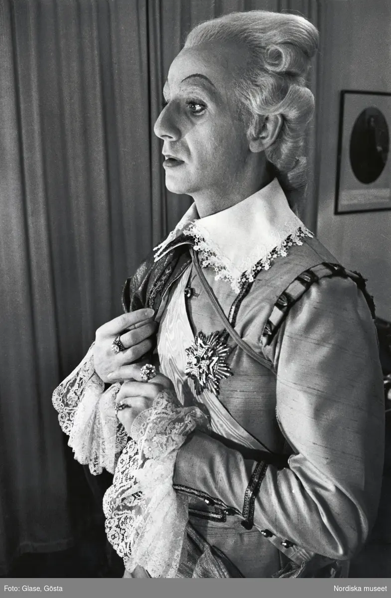 Porträtt av skådespelaren Jarl Kulle (1927-1997) som kung Gustav III.
Kulle står i halvprofil iklädd en version av den svenska dräkten med spetskrage och spetsmanschetter. Snett över bröstet ett ordensband och på bröstet fäst en kraschan. På fingrarna bär han ringar med glitrrande stenar. Porträttet är troligen från Kulles medverkan i Dramatens uppsättning av Strindbergs Gustav III, 1963.