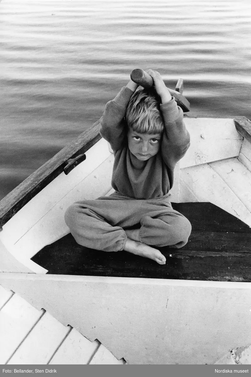 Fotografens son Tom sitter i en båt med rodret över huvudet.