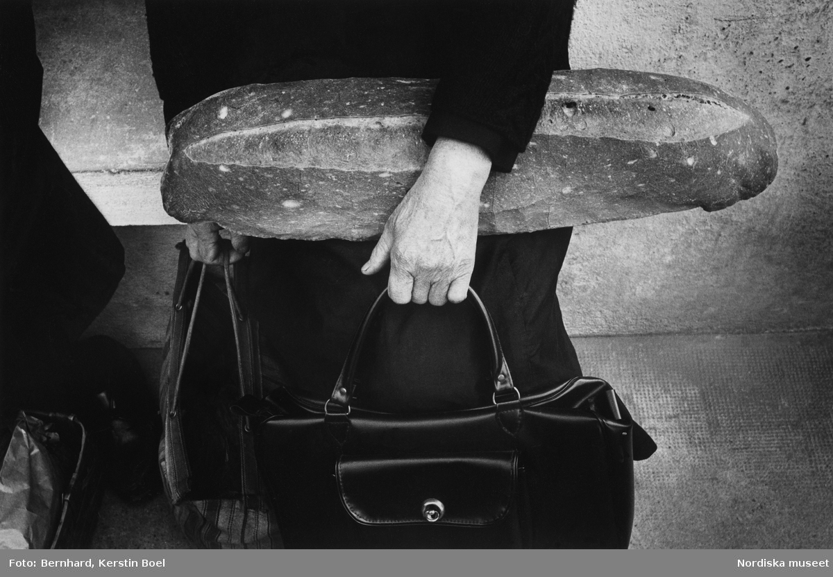 Kvinna som håller i två väskor och ett stort  bröd.