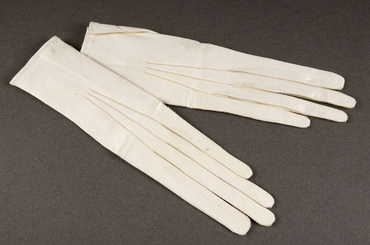 Ett par handskar av vitt glaceskinn, ofodrade, sydda med kastsöm. Knäppta med liten mässingsknapp. Stämplade med rött: F. Krook Silvermedalj 1860 Göteborg 6 ½.