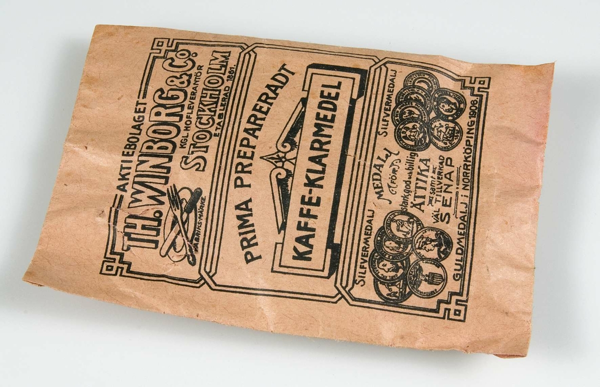 Rosa papperspåse innehållande klarmedel till kaffe. Svart tryck: "PRIMA PREPARERADT KAFFE-KLARMEDEL" samt AB Winborgs fabriksmärke. På baksidan reklam för Winborgs ättiksprit. 