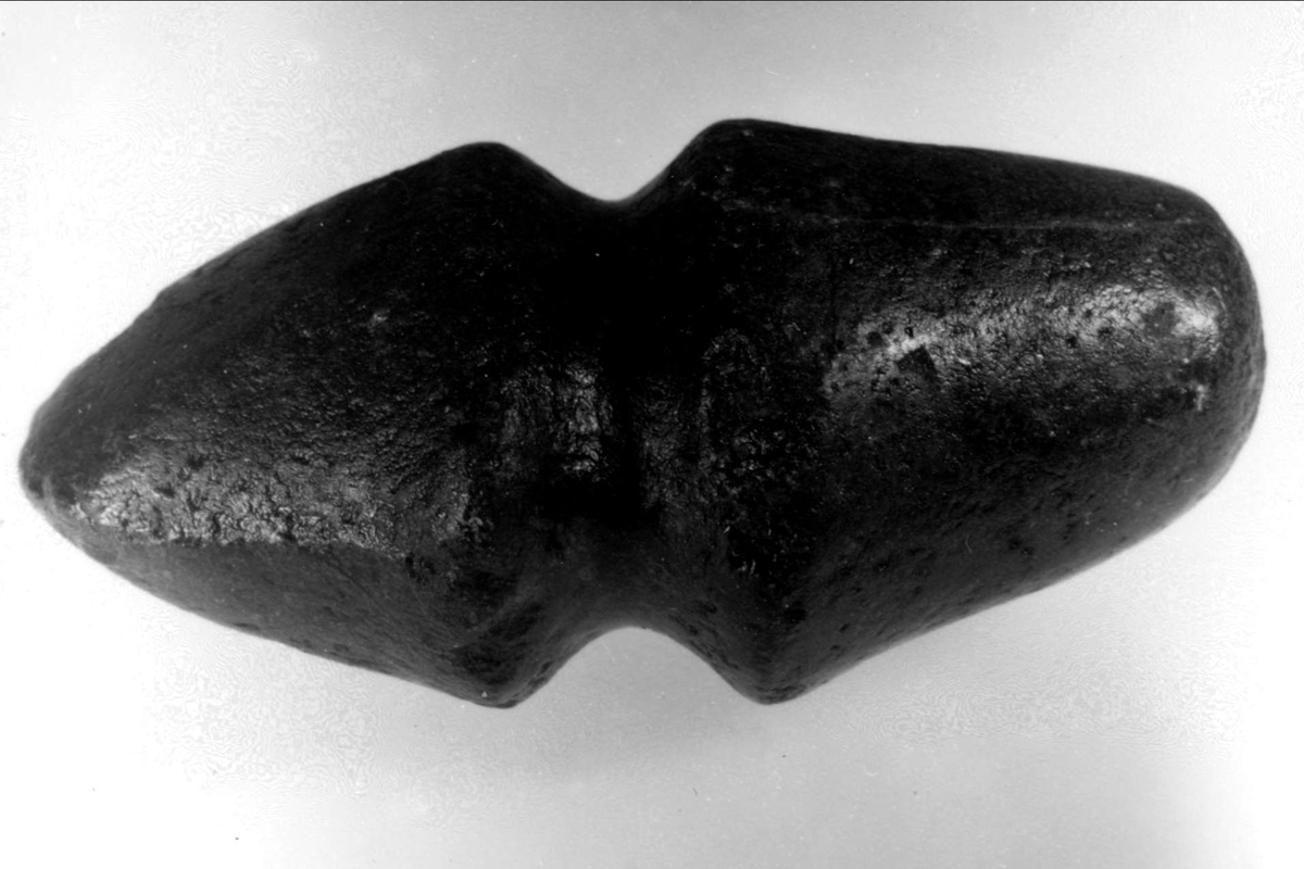 Klubba av sten. Klubban är tunnare och har symmetriska avfasningar i ena änden medan den andra änden är jämnt avrundad.