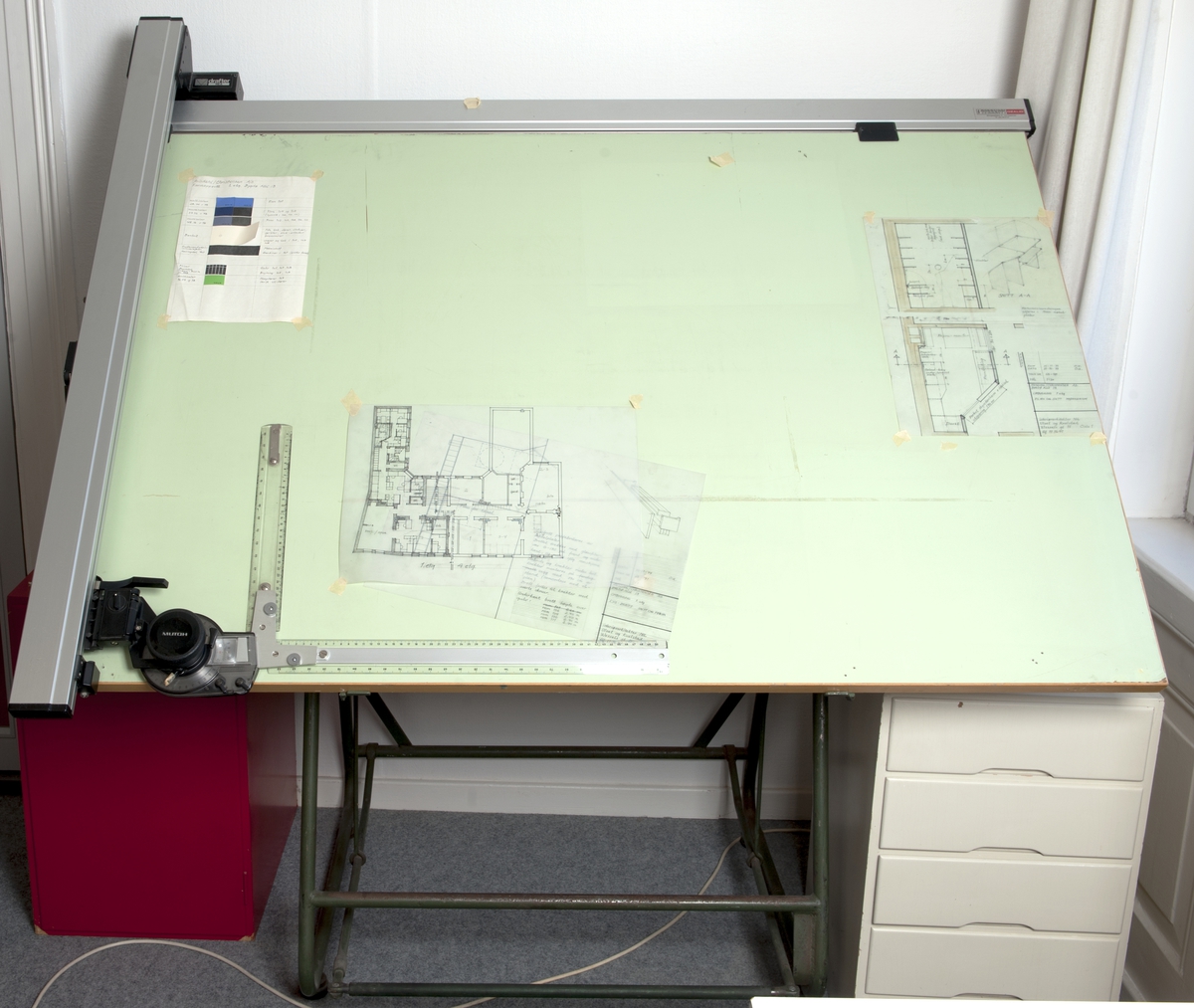 Tegnebord med regulerbar bordplate; blekgrønt plastbelegg/trekk. Påmontert tegneutstyr.