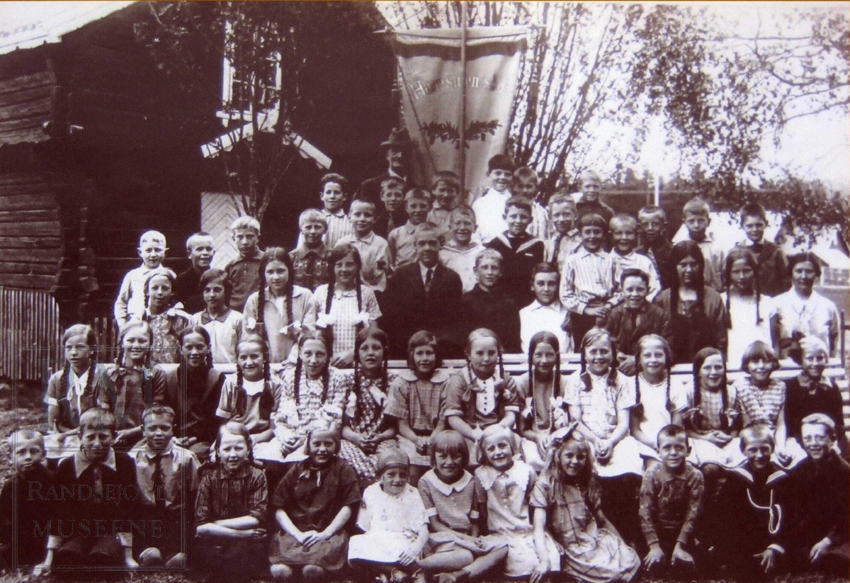 Klassebilde 1. klasse Harestua skole ca 1925 ved stabbur med fane i bakgrunnen.