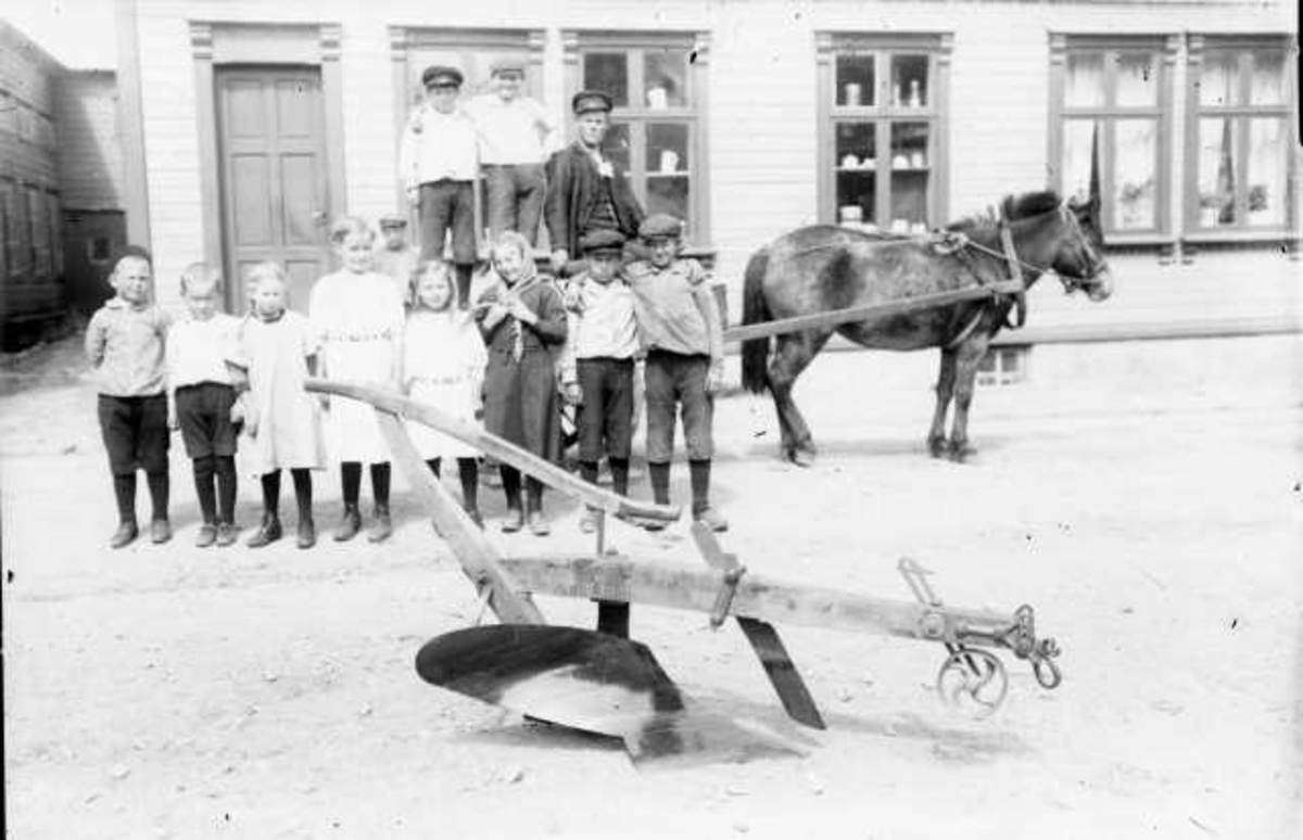 Gruppe av barn foran en hestevogn i Nærbø, utenfor handelsmann Adnesen nr.3 f.v. er Berta Opstad, framme plog
