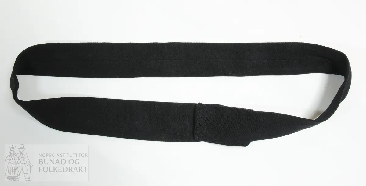 Belte sydd i svart, mjukt toskaft-vove ulltøy. Vransydd med saumen omlag midt på på baksida av beltet. Lukking med to par trykknappar.