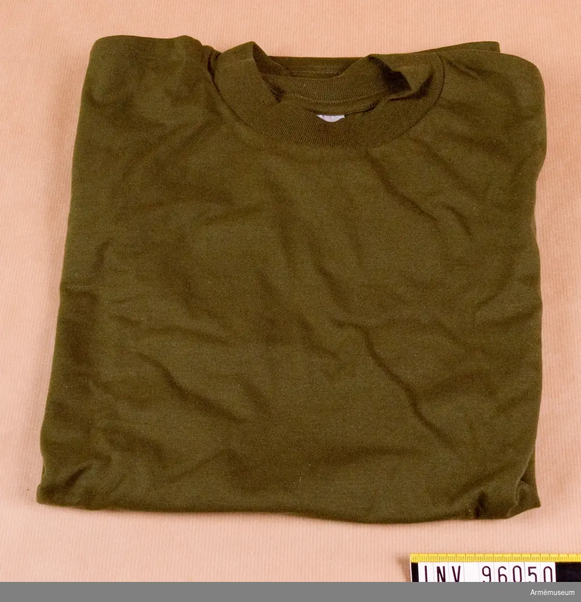Kortärmad, grön, t-shirt, stickad av 100% ringspunnen bomull. Tröjan är tillverkad i singeljersey med halsmudd i 1:1 ribb. Tröjan låg förpackad tillsammans med ytterligare 5 i en polyetenpåse med etikett: "Arbetsmodell, T-shirt grön, M7321-161000-4, Eva Berglund, FMV:IntT 1995-04-11".