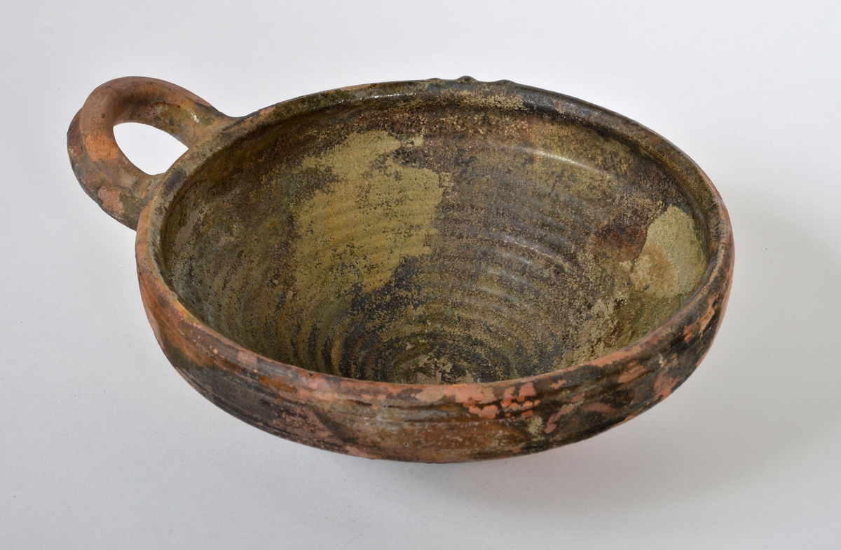 En skål av keramik. Skålen är försedd med en hänkel.