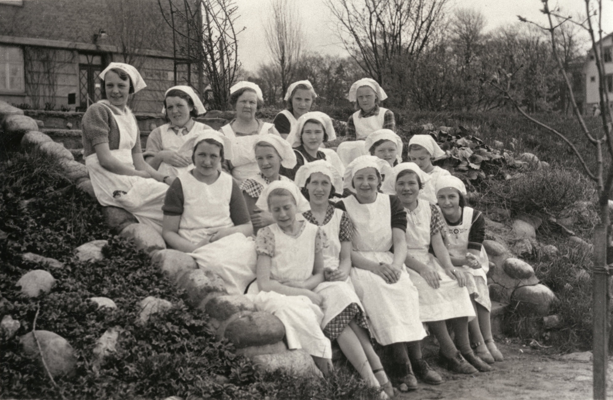 Flickor iklädda skolkökskläder, sittandes på trappan till Kvarnbyskolan (f.d. Centralskolan), cirka 1935.