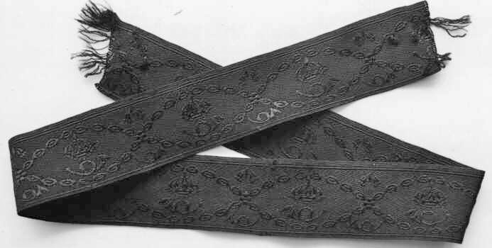 Mössband av svart silke med invävda bladrankor, posthorn och kronor. Mössbandets bredd ska enligt beklädnadsreglementet vara 40 mm men är således 5 mm smalare.
