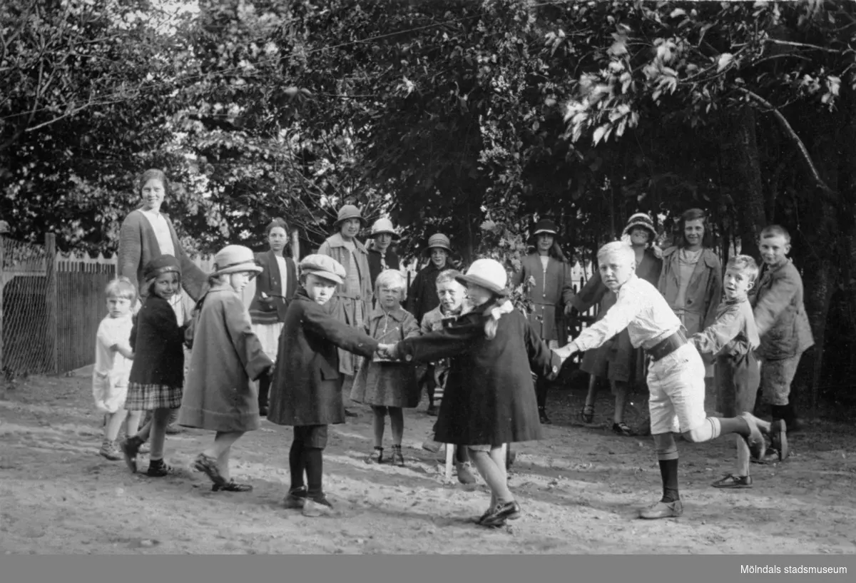 Midsommarfirande på Kvarnbygatan 23, 1920-tal. 
Den stora flickan längst till vänster är Astrid Andersson. Barnen i främre raden är: nr 2 från vänster Lisa Malmberg (i sjömansmössa), nr 5 är Margot Fässberg (g. Dalkvist), nr 6 är Pelle Malmberg (ljust klädd, brett bälte). Ovanför och något till vänster om Pelle Malmbergs huvud ses Tyra Johansson (t v) och Annika Lövberg (t h). (Lisa Malmberg föddes 1917).
