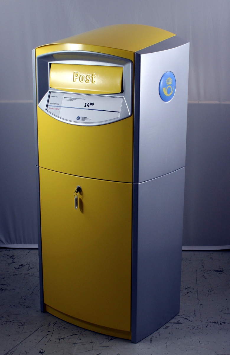 Brevlåda av den typ som infördes 2001-2002, gul med silvergrå sidor. På sidorna finns även Postens nya symbol ett gult krönt posthorn på en ljusblå cirkel. Brevlådan töms från fronten. Nyckel finns.