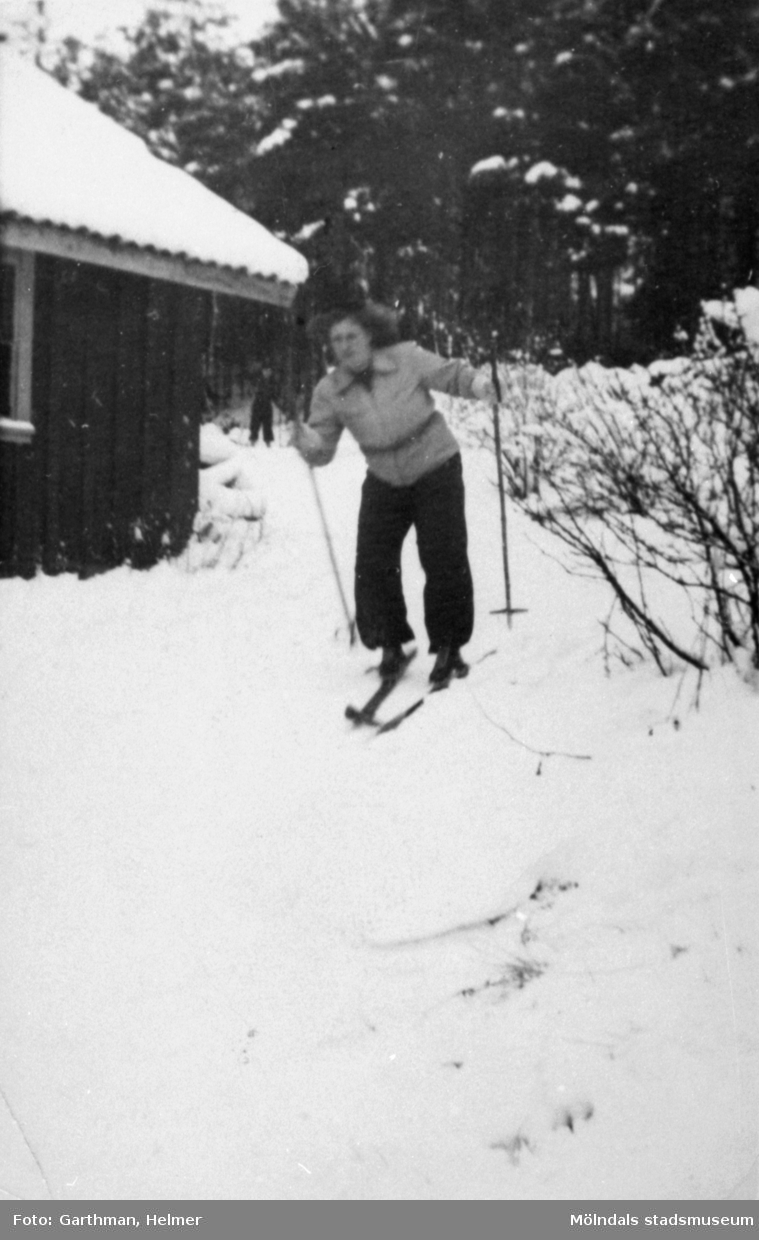 Astrid Garthman åker skidor förbi ett litet hus i Fjärås, 1930- 40-tal.
