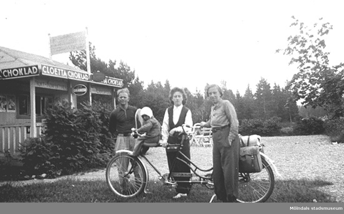Cykelsemester på tandem i Bohuslän för syskonen Rolf (i korgen) och Astrid Karlsson (gift Garthman) samt deras mor Alma. Längst till vänster står Astrids dåvarande fästman. Astrid är givarens mor och Alma Karlsson är mormor. 1930-tal.
