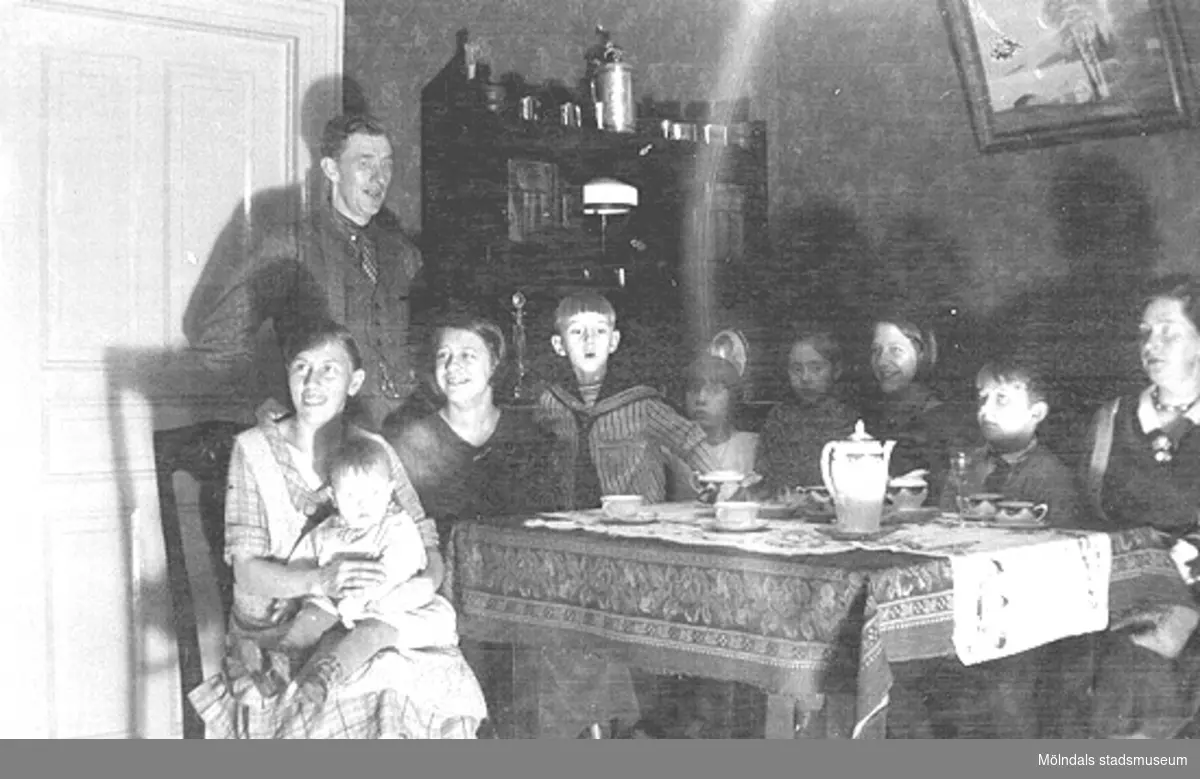 Julafton firas hemma hos familjen Karlsson på Kvarnfallet 31, 1930-tal. Från vänster Alma Karlsson med sonen Rolf i knät, Viktor Karlsson, barn samt släkt runt ett bord i vardagsrummet.