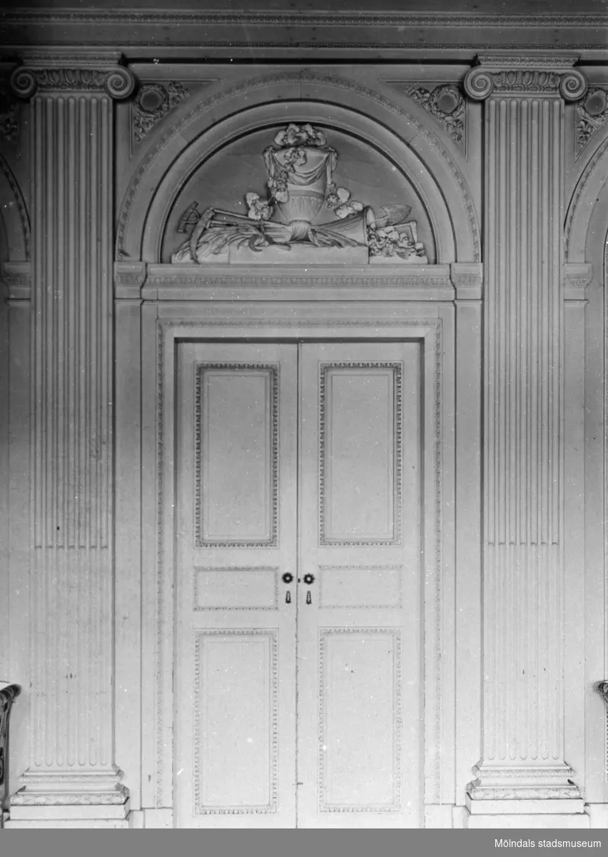 Dubbeldörr, mellan Salongen och Ovala vestibulen, med relief i halvcirkel ovanför. Reliefen föreställer en pokal med skäror och trädgårdsverktyg. Gunnebo slott 1930-tal.