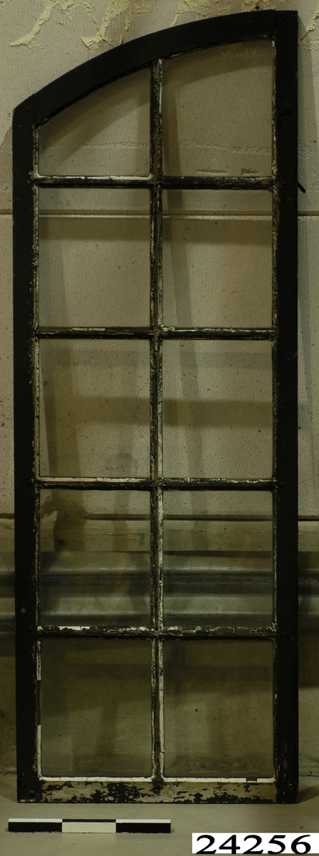Spröjsat fönster med tio glas inom ram av trä. Ramens överdel är bågformad. Ramen har svartmålad utsida och omålad insida. På insidan finns 3 haspar. Vitt kitt runt glasrutorna.