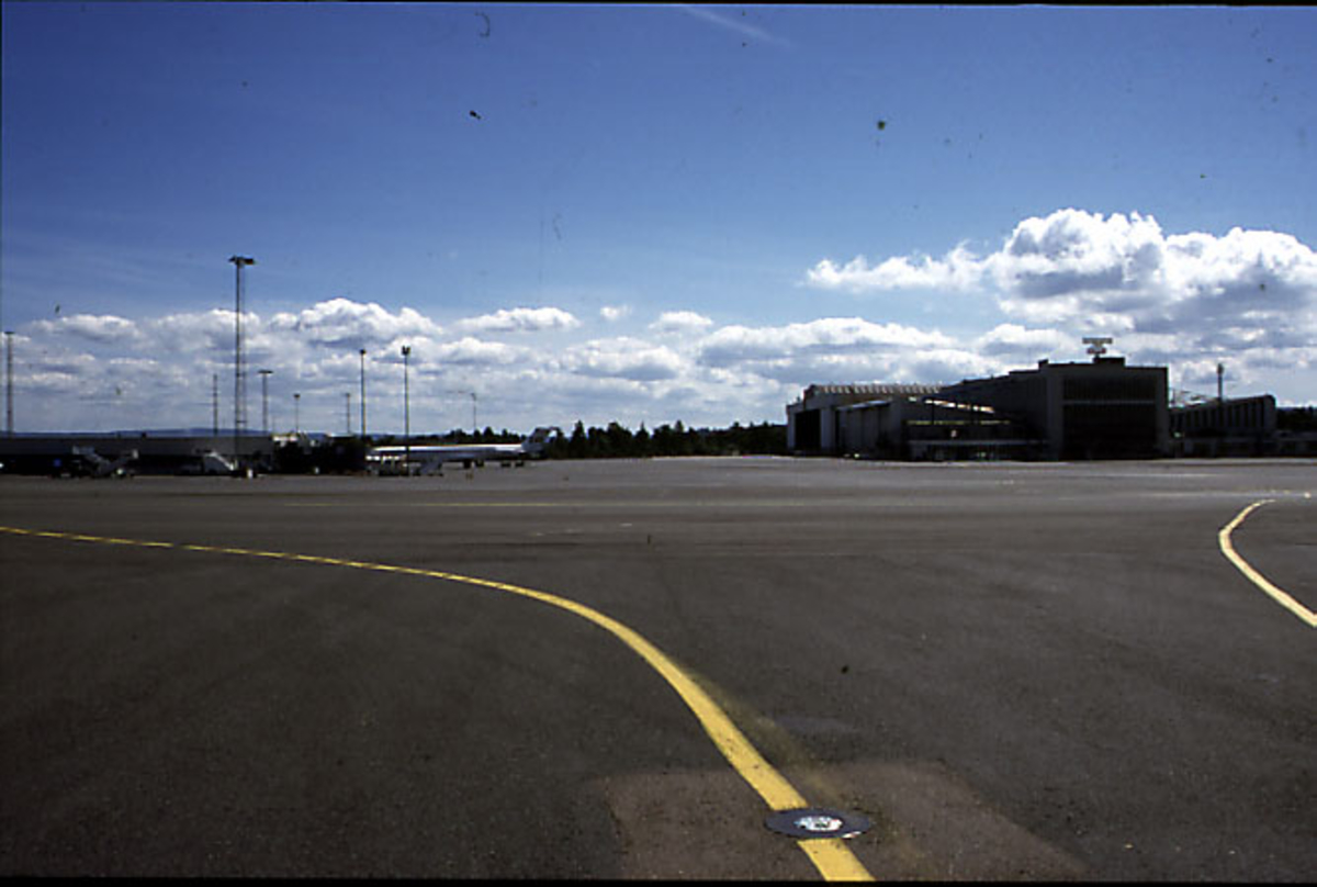 Lufthavn, litt av rullebanen i forgrunnen, terminalbygningen bak.