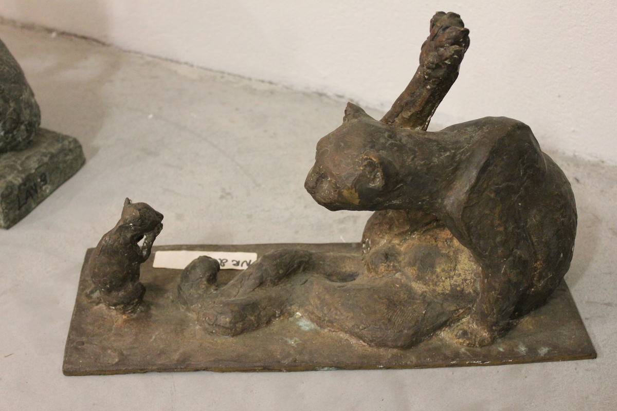 Skulptur i bronse av en katt som vasker seg. Tittel: "Pus vasker seg og mus ser på"