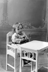Studioportrett av liten gutt som sitter ved et bord.