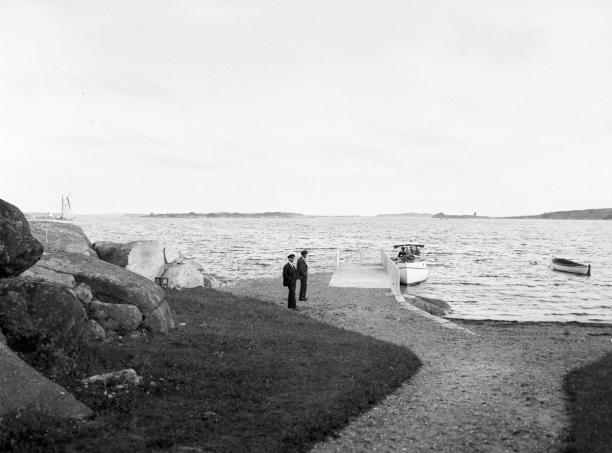 Strand og brygge på fritidseiendommen til Adolf Gundersen. Buvik, Slevik. Båt ved brygga, og to menn ved siden av.