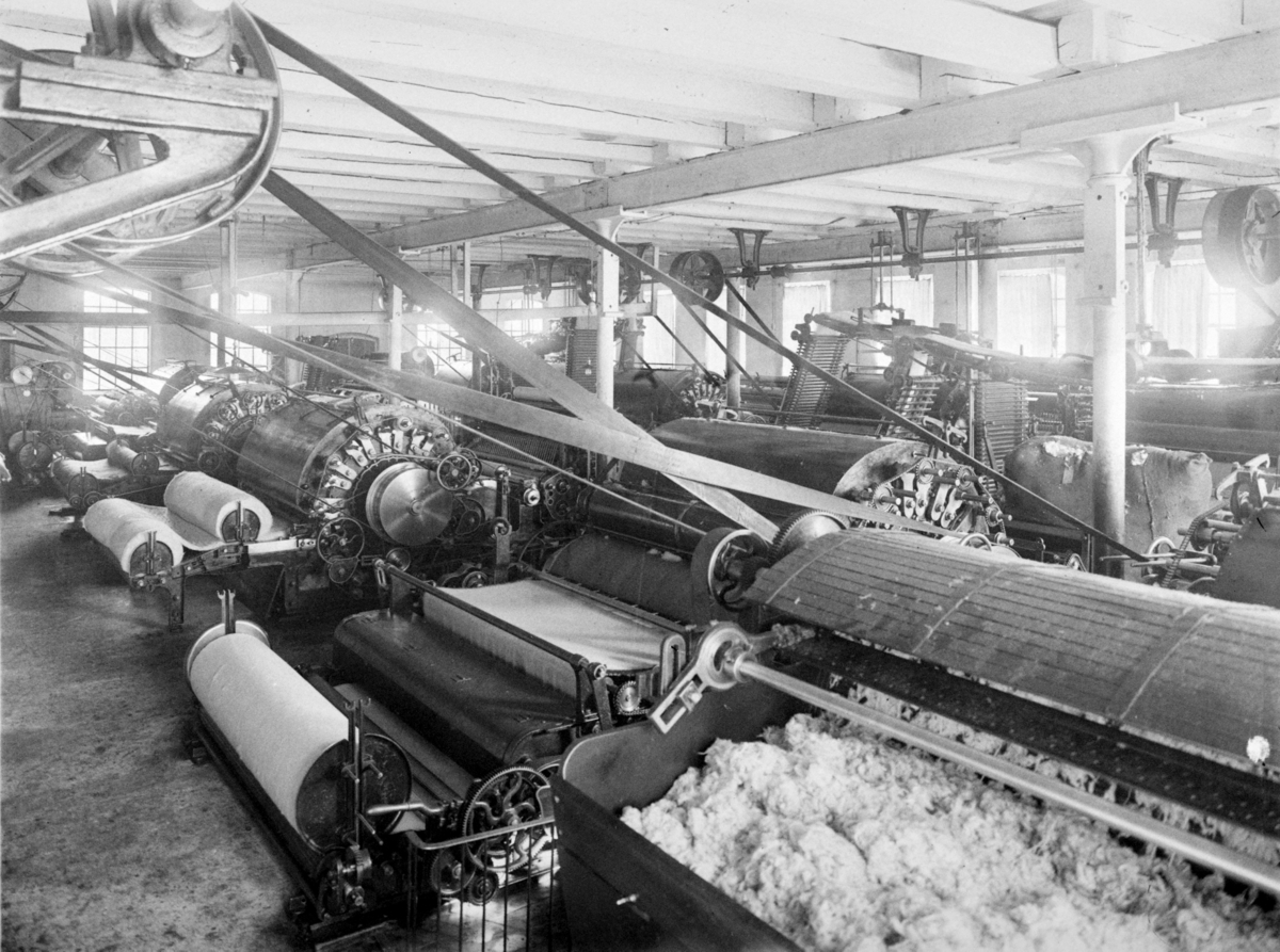 Interiørbilde av maskineri og ull ved A/S Det norske Cheviotspinderi som var i drift fra 1903 til 1958.