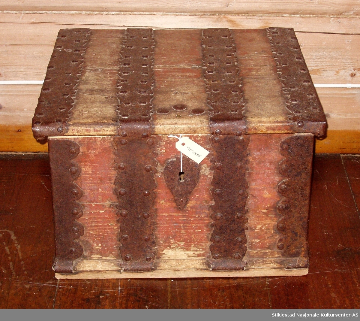 Firkantet kiste med alle hjørner beslått med jernbeslag. Flatt lokk. Det mangler nøkkel til låsen. Fra 1700-tallet, Tilhørt lærer Peder Brønstad.