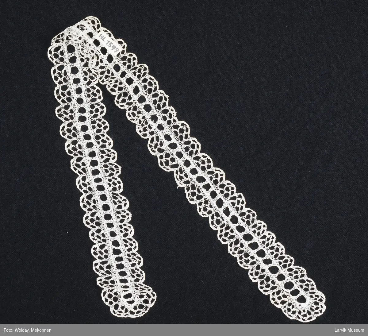 Form: fin,hvit tråd,ant. lin,håndstrikket i kniplings- mønster,sammensatt av et midtparti med regelmessige hull (11 hull pr. 10 cm), rundt det hele en bord av 7-hullsblomster
