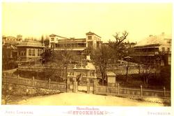 Prospekt over bygninger i park, gjærde med port og portnerbo