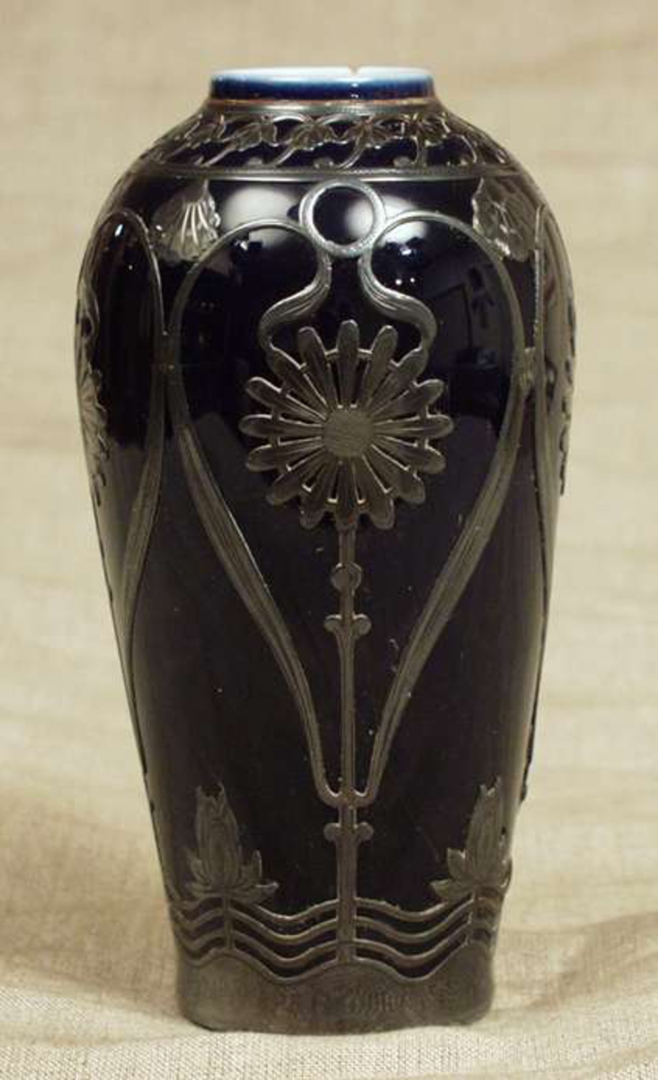 Vasen har blomsterdekor i metall. 