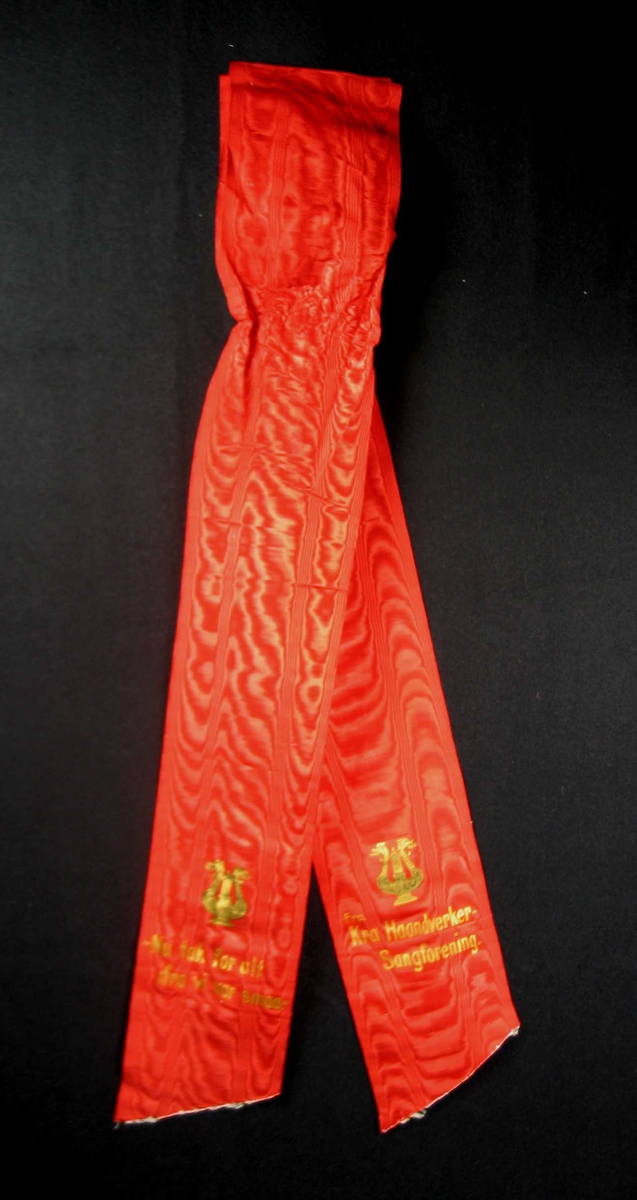 Begravelsessløyfe i mønstret rød silke med tekst i gull.