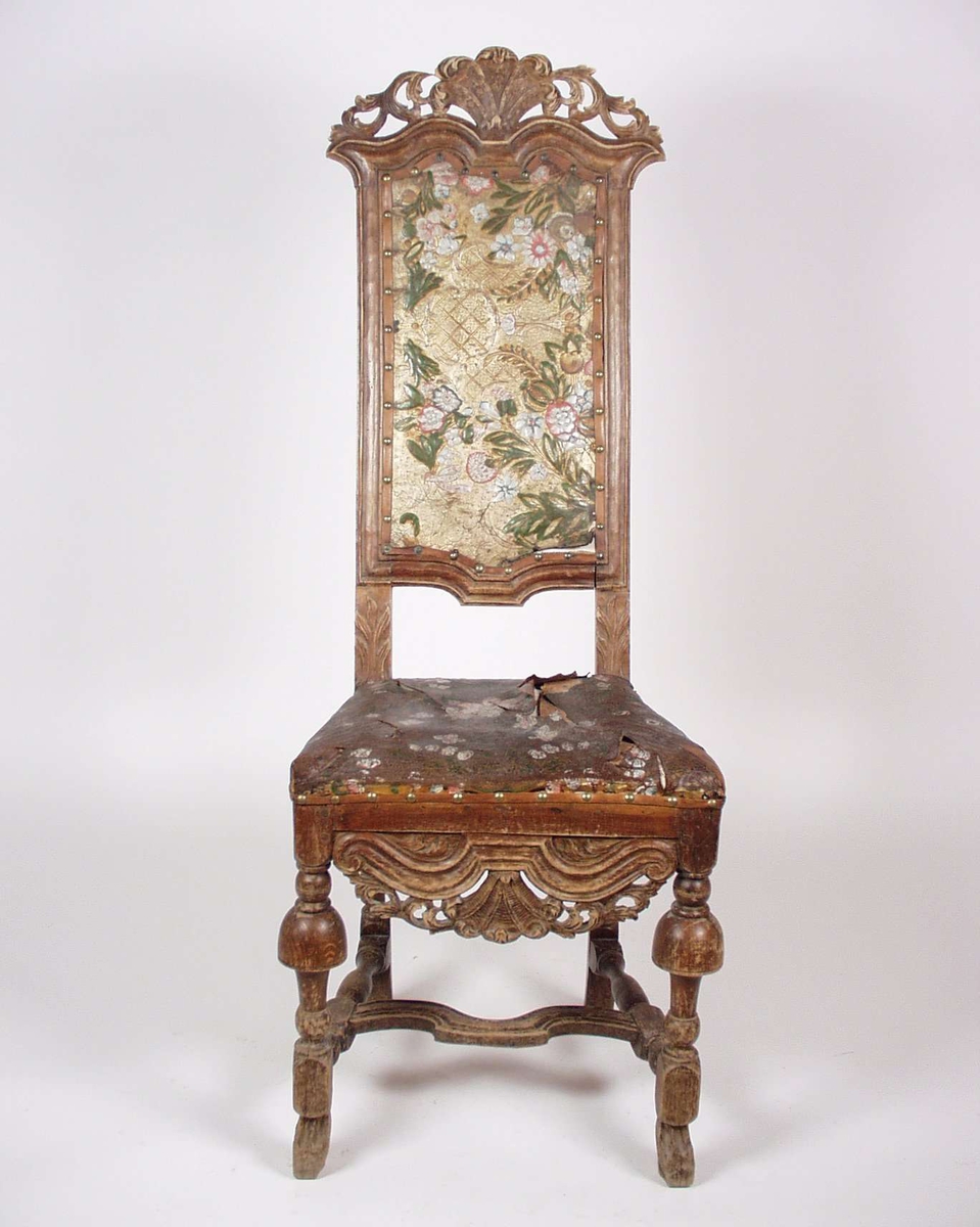 Stolen er av bøk med gyllenlær i sete og rygg. Stolen er rikt utskåret og gyllenlæret er dekorert med blomstermotiv.