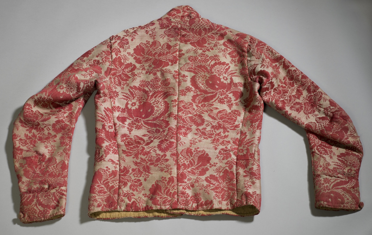 Håndsydd vest av ulldamask, fôret med to typer linstoff. Ryggsømmene er sydd med spilesøm. Vesten har ståkrage, dobbel knapphullrad (18) , trekte knapper (to ulike stoff) (16) - to mangler. Det vil si ni knapphull  og knapper på hvert forstykke. Knapphullene er sydd med lintråd.
To sidelommer. Knapp og knapphull nederst på ermene.